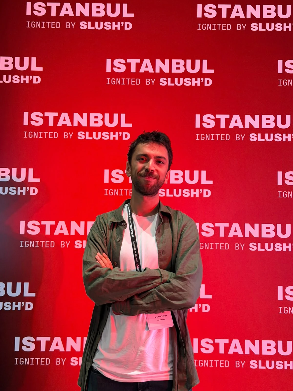Berke Çelik, “Istanbul Ignited by Slush'D” yazılı kırmızı panonun önünde kollarını kavuşturmuş hâlde